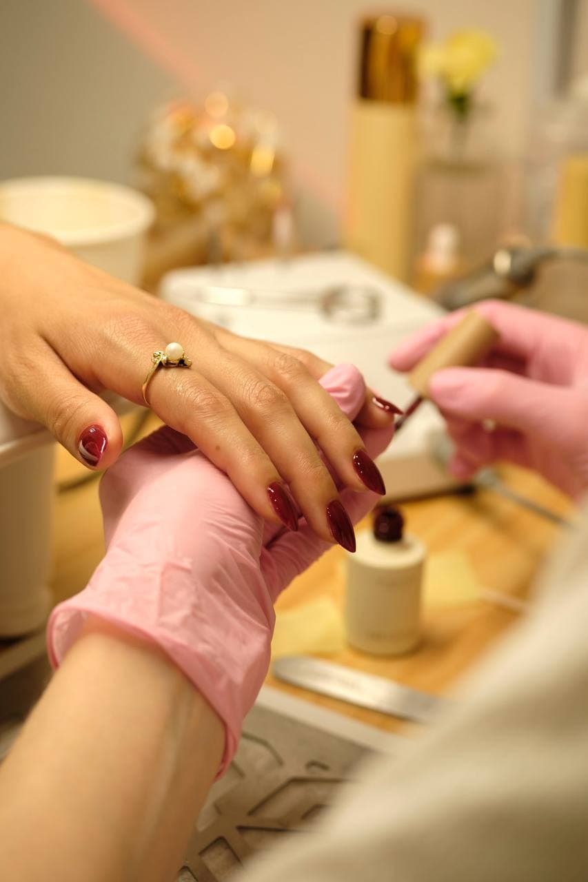 Applying dark burgundy nail polish — warm bokeh background