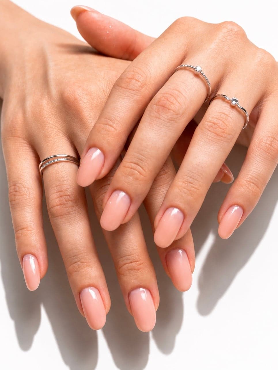Russian manicure with nude gel polish on almond nails, hands with silver rings